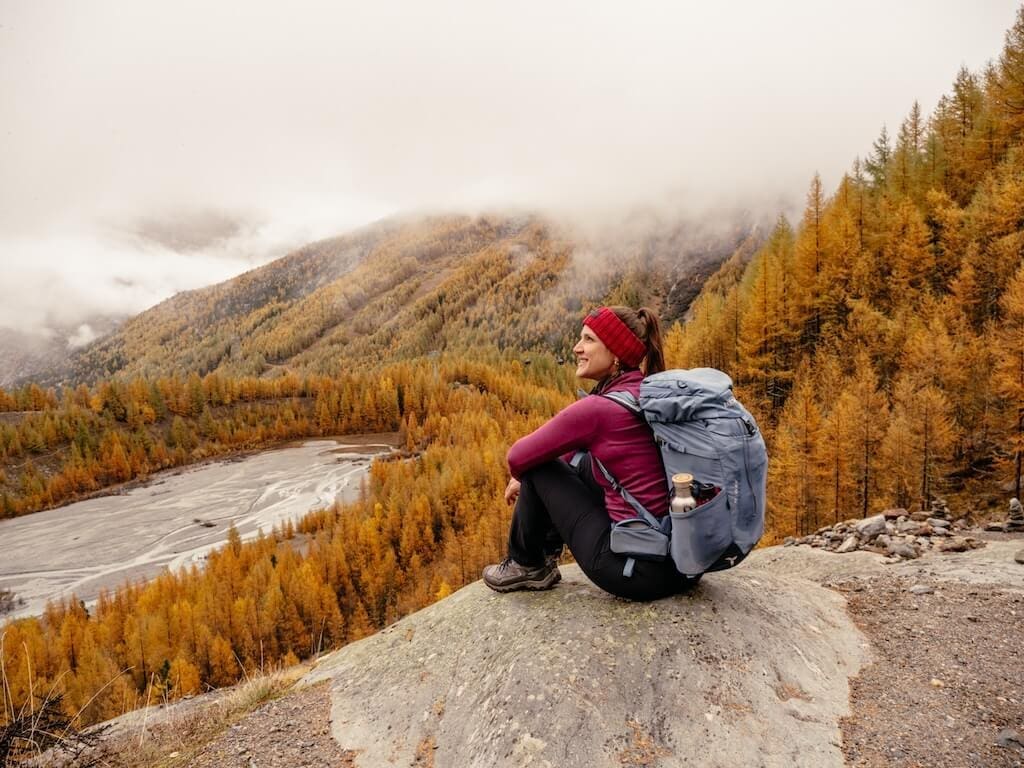 2024-10-Saas-Fee-2-Abenteuermomente-24 Person sitzt am Gletschersee zwischen Lärchen